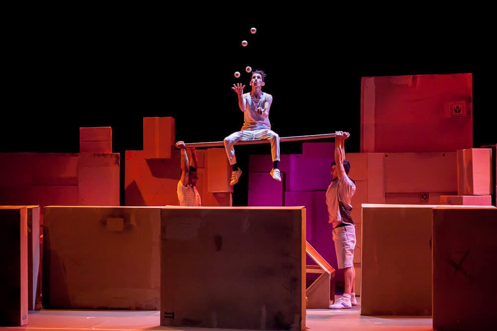 Artista de circo realizando equilibrios y malabares técnicos en altura sobre cajas.